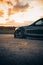 Sleek sports car parked in a parking lot with a stunning backdrop of a sunset in the background