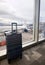 A sleek suitcase stands before a large airport window, offering a view of an aircraft and the expansive tarmac. It's