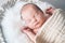 Sleeping newborn baby in basket wrapped in blanket in white fur background. Portrait of little child one week old