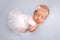 Sleeping newborn girl in a white ballet dress with a white bandage and a blue flower.Portrait of a newborn ballerina.