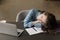 Sleepy exhausted student girl leaning head on table at laptop