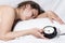 Sleepy girl can not wake up from the alarm bell. A woman is sleeping in bed and holding an alarm clock in her hand