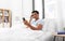 Sleepy indian man in bed looking at smartphone