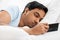 Sleepy indian man with smartphone lying in bed