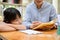 Sleepy little Asian girl leaning on the table while her private math teacher teaching