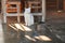 Sleepy white cat with dark tail resting under the table near wooden chair, morning sun shines on floor next to her