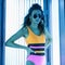 Slender beautiful young woman hipster in fashionable sunglasses in a colorful swimsuit with curly hair sunbathes in a solarium.