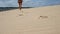 A slender blonde in a blue bikini walks along the sandy beach