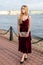 Slender blonde girl in elegant burgundy ankle-length dress looking away on the embankment