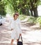 slender blonde girl in sunglasses, light shorts and a vest walks near a white car