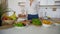 Slender blonde woman completes preparation of healthy breakfast and spreads vegetables, standing at table of modern