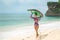 A slender brunette girl is walking along the beach, carrying a surfboard on her head