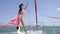 A slender brunette stands on a yacht floating on the sea in her heels and a bathing suit covered with a pink shawl under