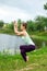 Slender Caucasian brunette girl doing yoga in summer on a green lawn by the river. Eagle Pose, Garudasana