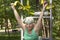 Slender elderly woman with gray hair conducts individual fitness classes on a simulator in a city park.