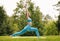 Slender focused girl performing yoga outside in early morning in park, standing in warrior pose