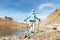 A slender girl backpacker with tracking sticks stands next to a high mountain lake high in the mountains of the Caucasus