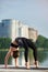 Slender girl in black sportswear practicing yoga outdoors near the river, standing in Upward bow Wheel pose