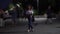 A slender girl in a blouse and hat stands among the crowd in the square in the evening, shot in blur timelaps