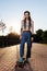 Slender girl with dreadlocks in jeans and a top rides a longboard at sunset