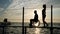 Slender girl with man disabled on wheelchair walking on pier at sea against sky in sunset