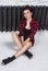 Slender girl in plaid shirt sitting on floor near black radiator