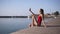 The slender girl sits on the pier near the water and makes selfie on her cell phone. Attractive model in a red swimsuit