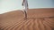 Slender girl in a white dress goes barefoot on the sand in the desert