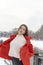 Slender girl in white knitted sweater and red short down jacket with knitted mittens poses in snow-covered park