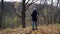 A slender man with gray hair stands on the edge of a ravine in the autumn forest and looks at a tall dry oak on a cloudy