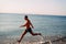 A slender muscular tanned guy in blue swimming trunks runs along the sandy shore of the ocean