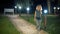 A slender, sweet middle-aged woman with curly blond hair walks down a green alley with lanterns on a summer evening