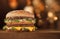 Slender tall double burger with meat and cheese on a wooden table with bokeh on the background