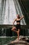 A slender tanned girl with a sports figure is doing yoga exercises against the backdrop of a waterfall