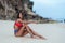 Slender tanned woman in colored swimsuit sits on ocean beach with white sand