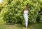 A slender woman with curly hair stands in a flowering bush