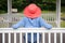 Slender woman in dark pink hat sitting on white bench in gazebo looking at her garden