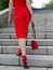 A slender woman in a red dress with a handbag climbs elegantly up the stairs, rear view