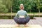 A slender woman sitting on a wooden platform by a pond on green mat in summer, does yoga