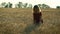 A slender woman walks on a wheat field, smiling and holding chamomile flowers in her hands on a Sunny summer day.