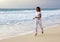 Slender woman in a white tracksuit jogging along the edge of the waves on the sandy beach of the sea