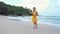 A slender young beautiful brunette in a yellow dress takes a selfie on the phone while walking along the beach by the bay.