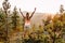 A slender young long-haired woman in a t-shirt and shorts stands with her hands up on the mountain