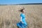 Slender young woman in a bright blue dress with long blonde hair fluttering in the wind in a field of golden wheat ears on a summe