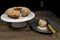 A slice of almond donut with buckwheat on a dark plate next to a white cake stand with the rest of the cake on top