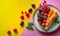 Slice of Berry peach raspberry cream cheese curd fruit tart tartlet pastry dessert on pink yellow background