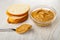 Slice of bread, spoon with peanut butter, transparent bowl with peanut butter on wooden table