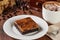 Slice of coffee chocolate brownie on a plate with a cappuccino on a wooden table