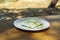 A slice of feta white cheese on a wooden table outdoors served on a dish garnished with oregano and olive oil