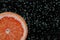 Slice of grapefruit in sparkling water on black, closeup with space for text. Citrus soda